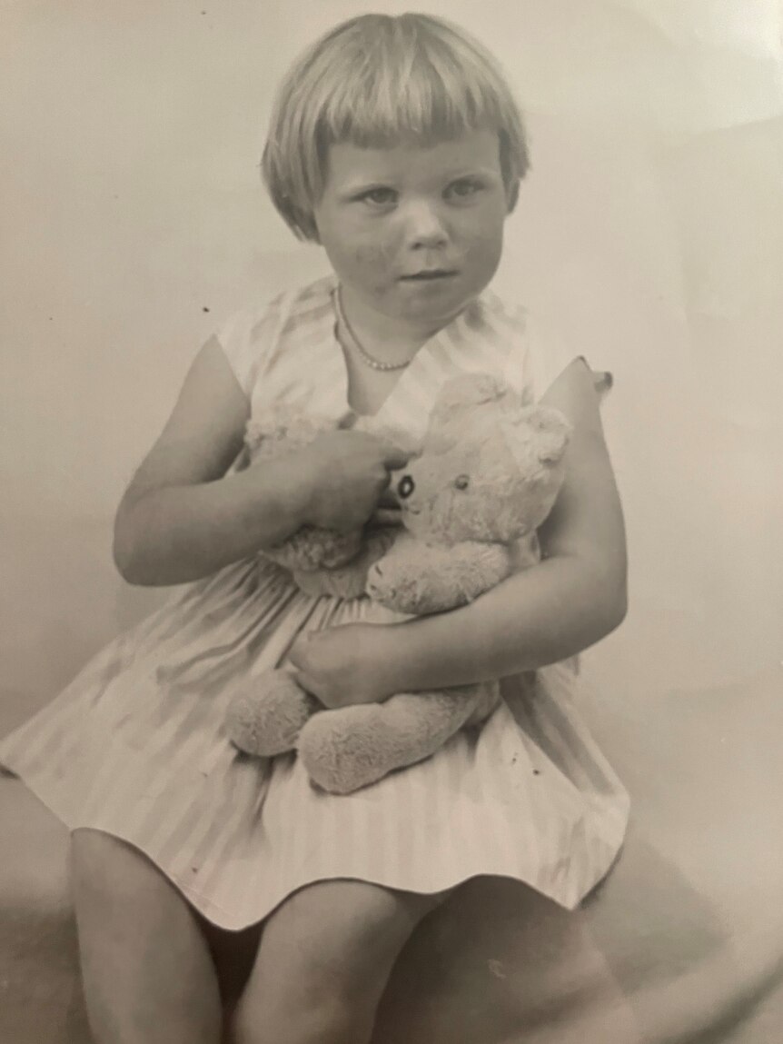 A black and white image of a young girl in the 1950s holding a teddy bear.