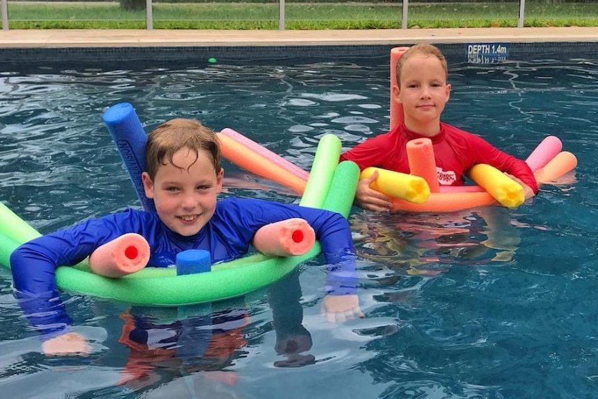 Two boys floating on colourful pool noodles in a pool for a story on bringing a premature baby home.