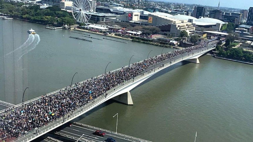 Thousands of people marching across a bridge over the Brisbane River