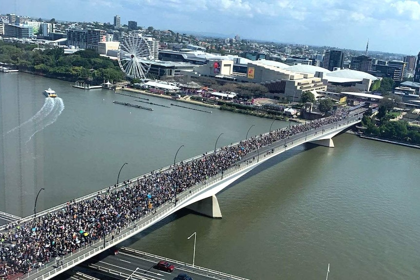 Thousands of people marching across a bridge over the Brisbane River