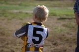 A young boy stands with his back turned wearing an Australian Rules football jumper with the number 5 on it.