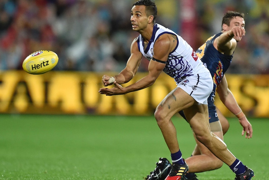Danyle Pearce of the Fremantle Dockers handballs a yellow football with an Adelaide Crows player behind him.