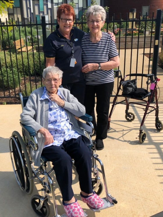 A aged care worker stands with two residents who are about to go for a bike ride