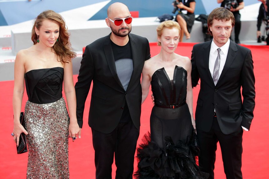 Two men and two women in evening wear pose for photos on the red carpet.