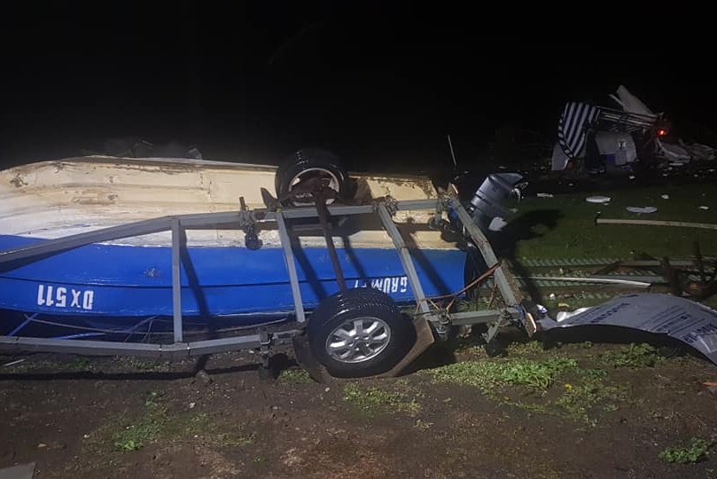 An overturned boat lies on a road, surrounded by debris