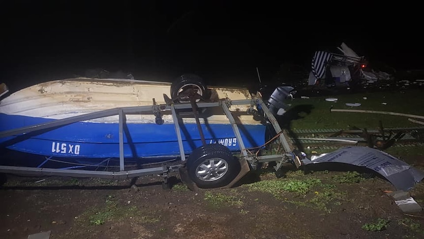 An overturned boat lies on a road, surrounded by debris
