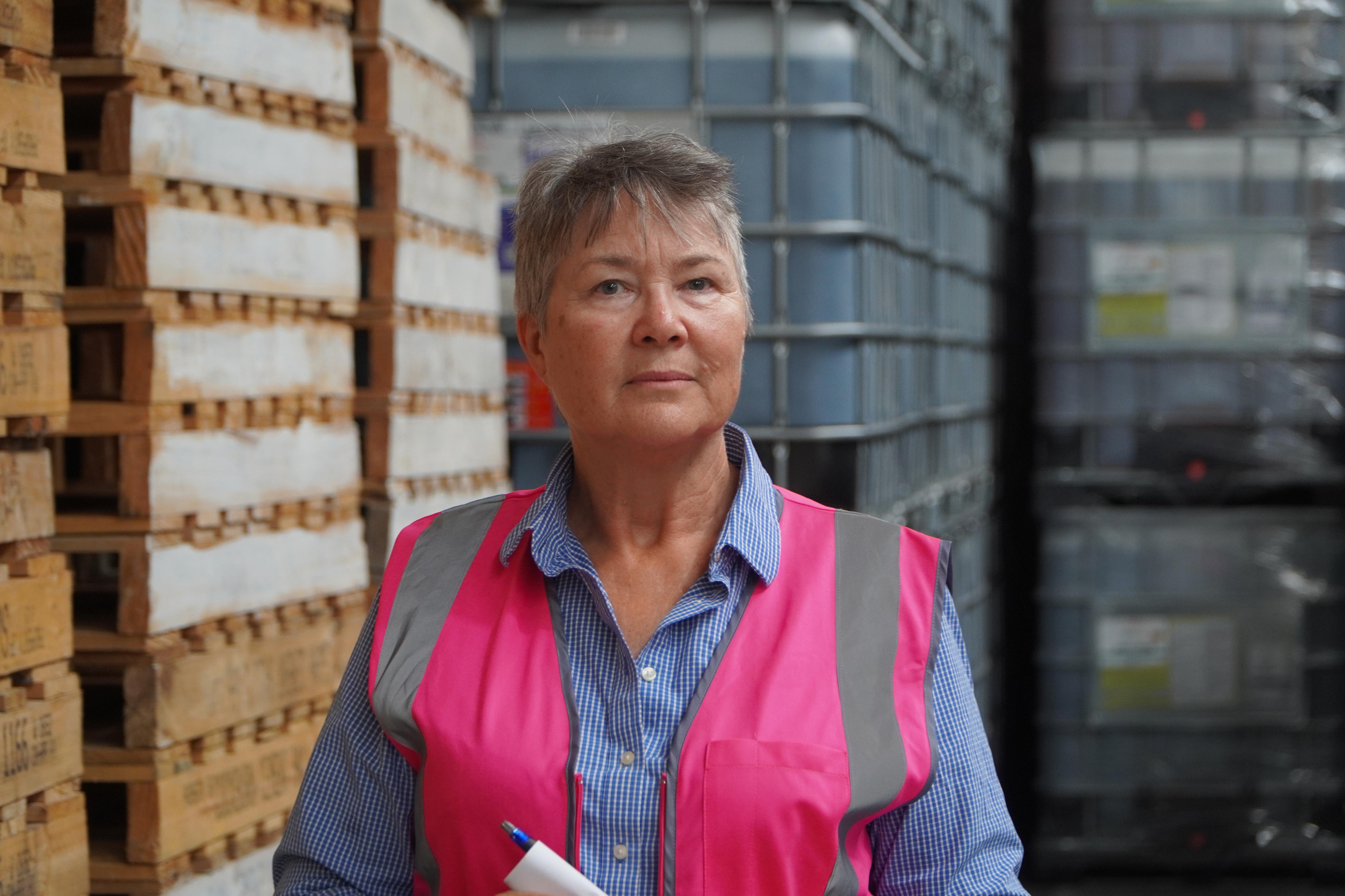 A woman wearing a pink high vis vest over a blue shirt looks straight at the camera. 