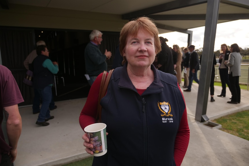 a woman stands outside a hall with a cup in her hand