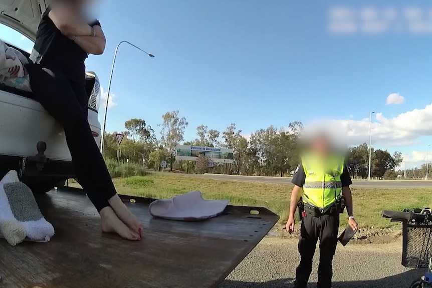 The stowaway woman stands with arms and legs crossed as police talk to her.