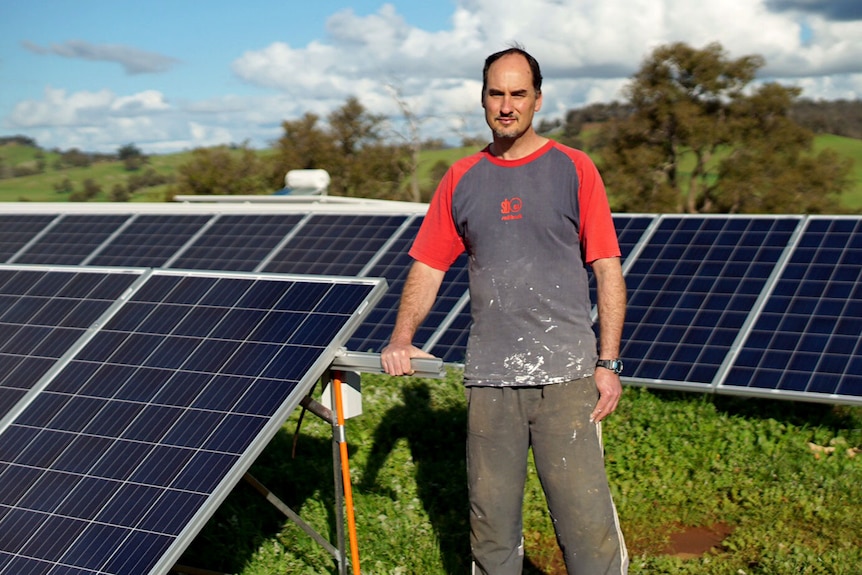 Doug McGhee stands among ground-mounted solar panels.
