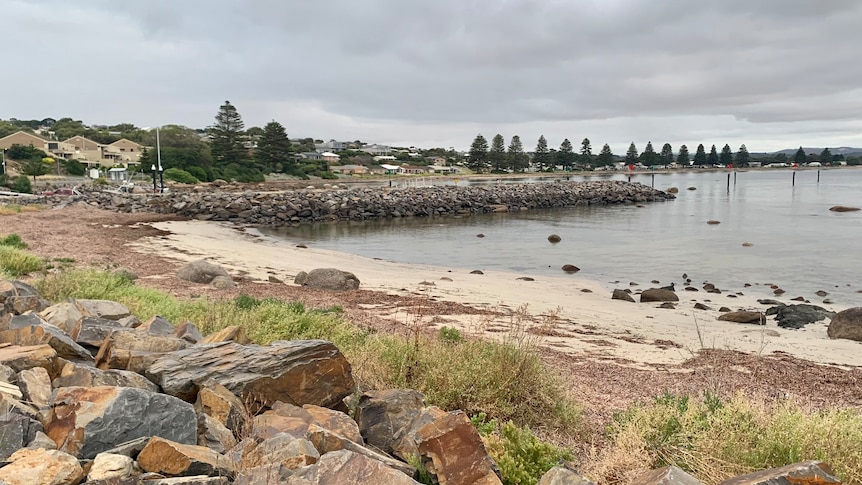 A small sandy beach next to a breakwater and boat ramp