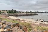 A small sandy beach next to a breakwater and boat ramp