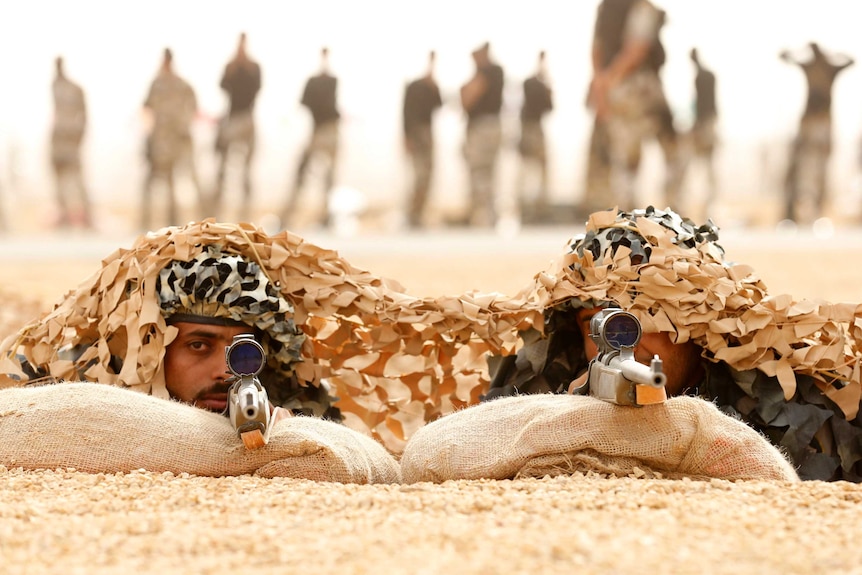 two men in camouflage aim guns at the camera