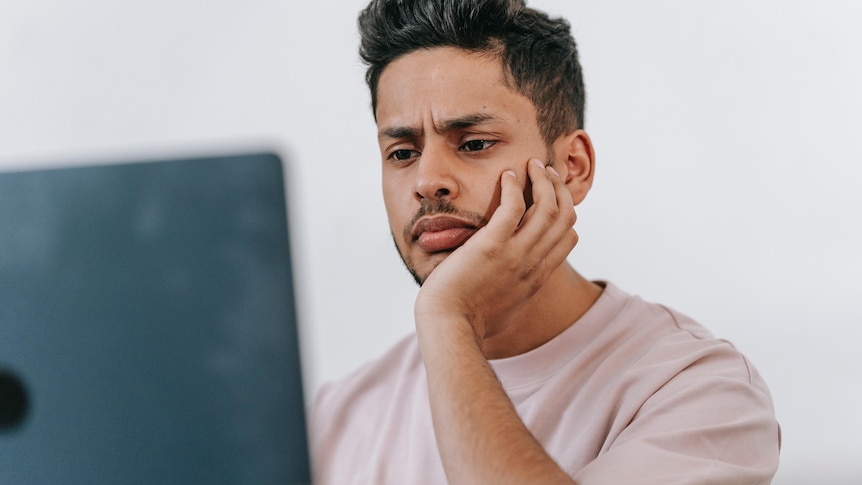 A young man looking confused in front of a computer.