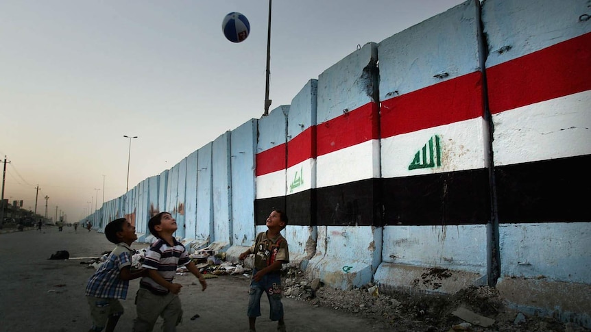 Iraqi children play football next to the security wall with an Iraqi flag painted on it