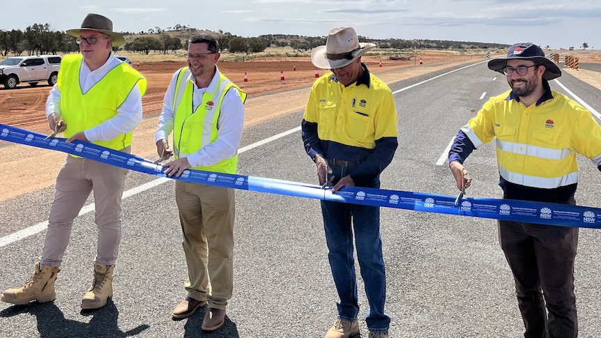 A line of men in fluro clothing cutting a ribbon on a road