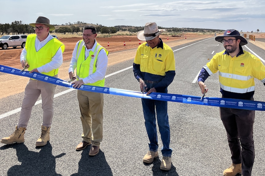 A line of men in fluro clothing cutting a ribbon on a road