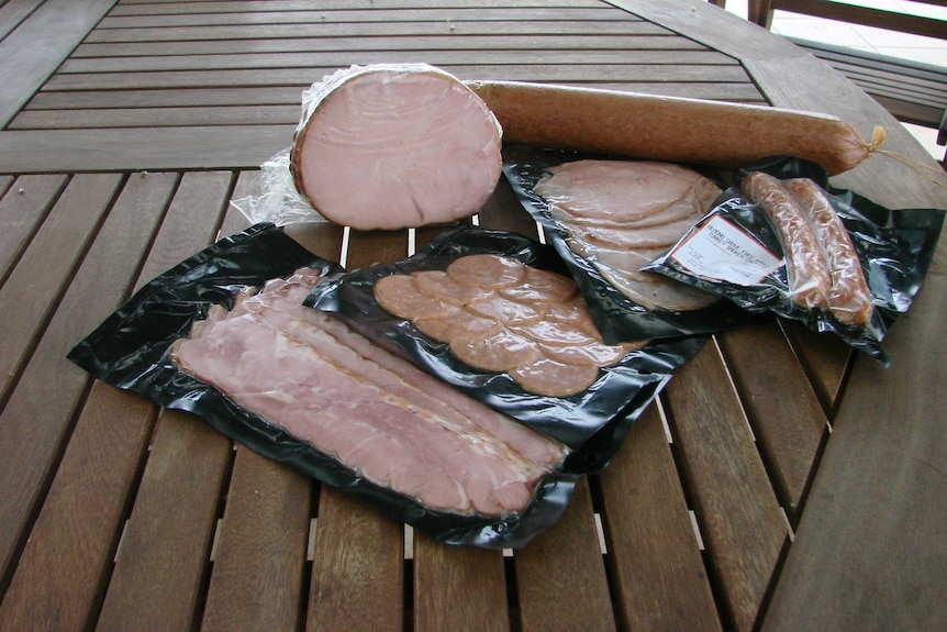 A variety turkey meats including sausages and bacon sitting on a wooden table