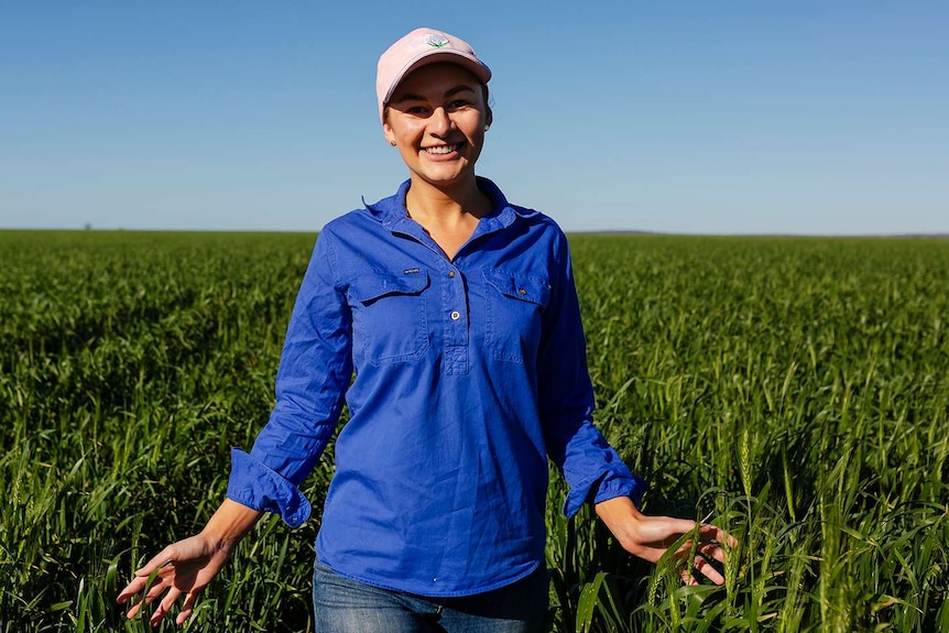 A young woman walks through a sorghum crop, running her hands through it as she goes. Blue sky in background.