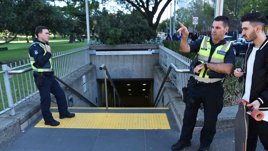 Police officers talk to a man with a skate board at Flagstaff train station entrance.