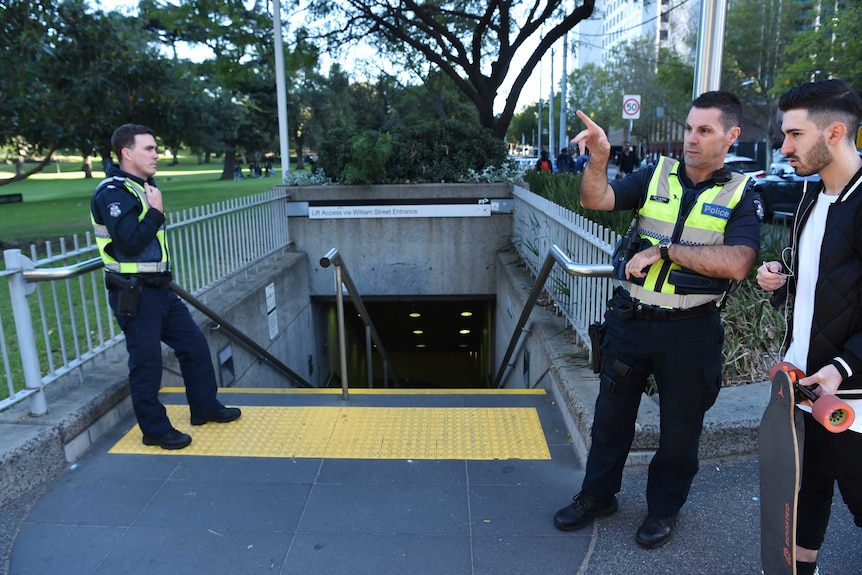 Police officers talk to a man with a skate board at Flagstaff train station entrance.