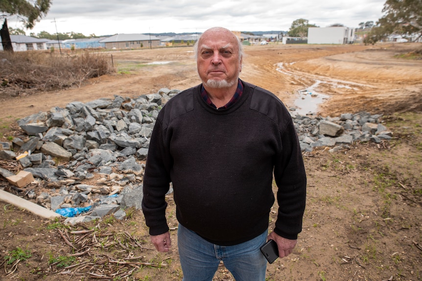 A man stands in front of a muddy block where houses are being built
