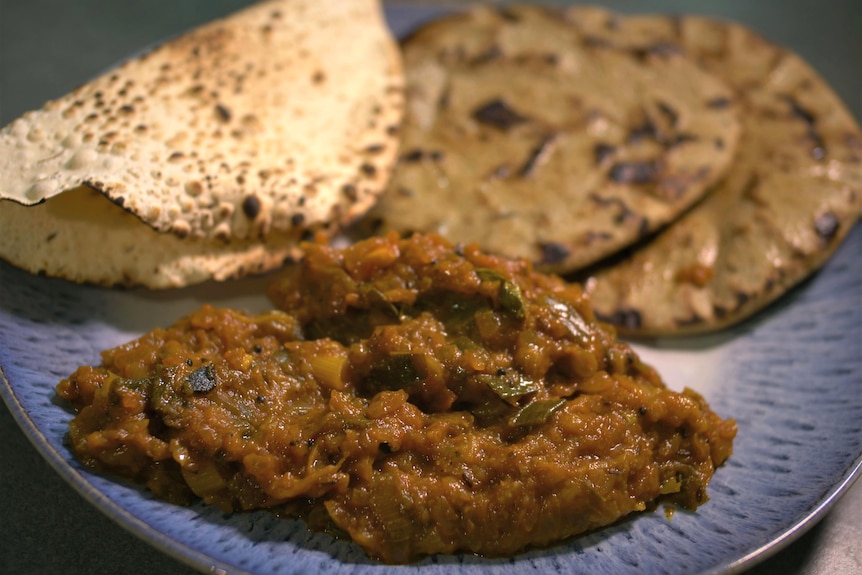 An Indian vegetarian meal on a plate, including curry, flatbread and pappadums.