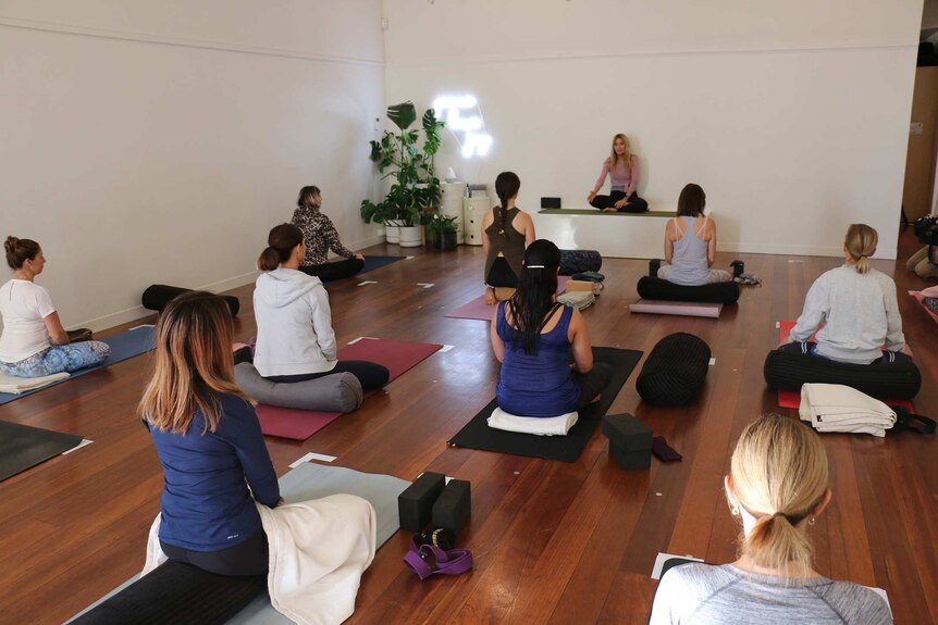 A wide shot of an indoor yoga class involving about 10 women.