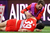 Paddy McCartin lies on the ground while a Swans club doctor helps him