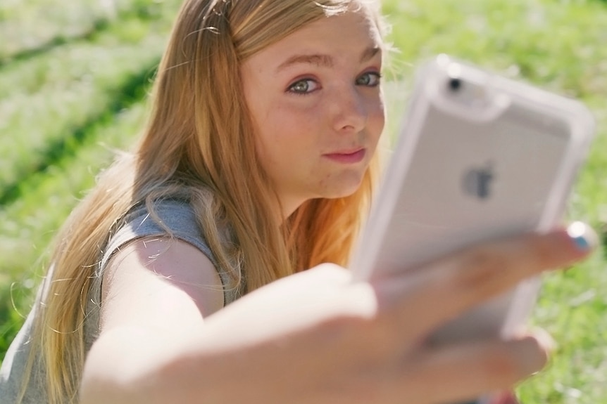 Colour still of Elsie Fisher taking selfie on a sunny day in 2018 film Eighth Grade.