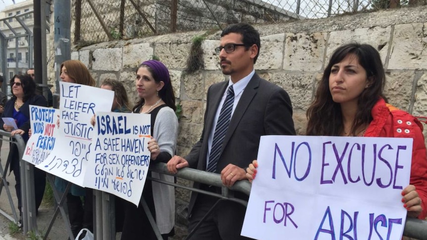 Protesters hold signs with messages about abuse in front of a brick wall at an Israeli courthouse.