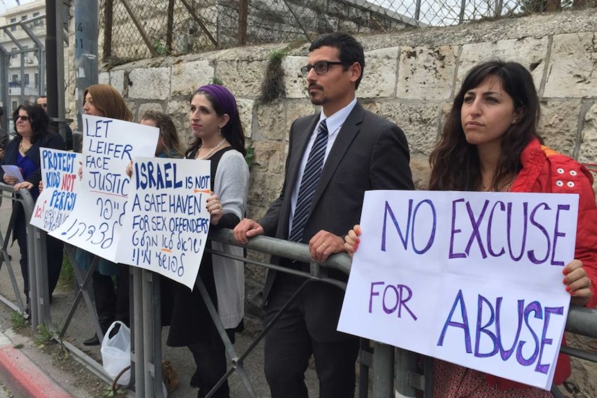 Protesters hold signs with messages about abuse in front of a brick wall at an Israeli courthouse.