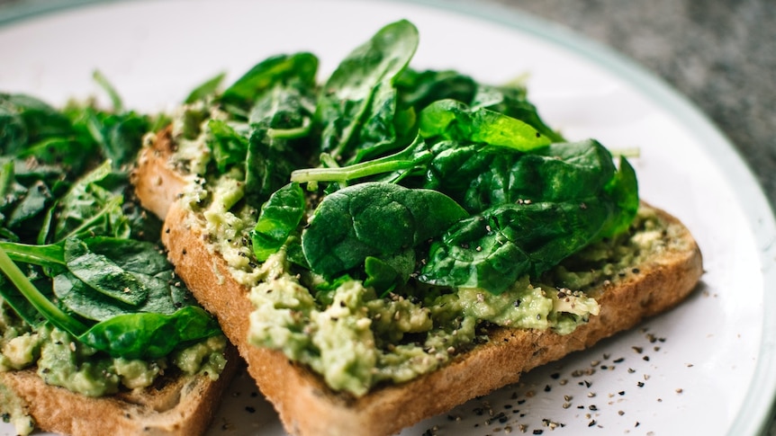 Smashed avocado on toast with fresh spinach on top and black pepper.