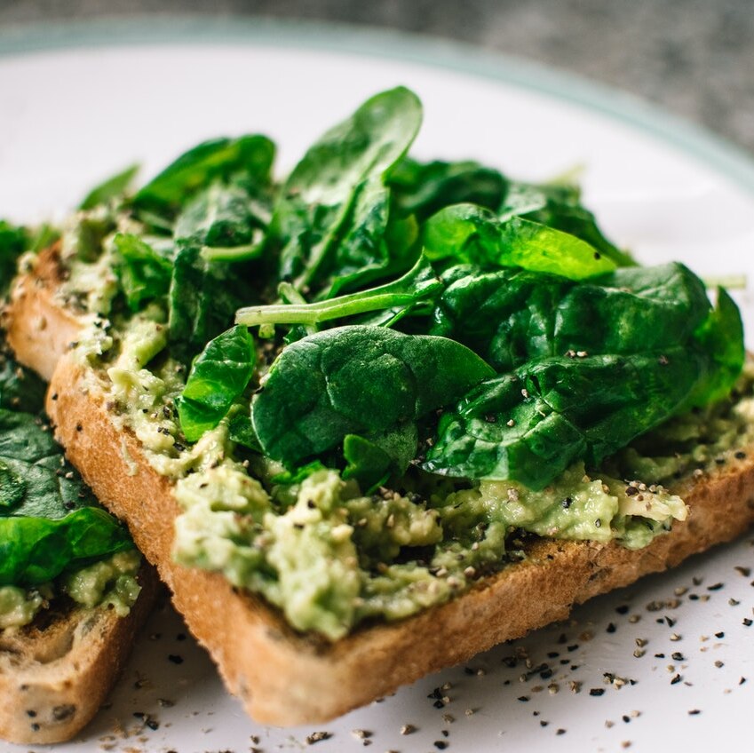 Smashed avocado on toast with fresh spinach on top and black pepper.