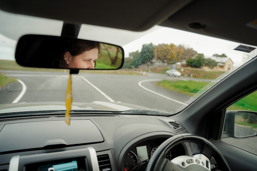 Julia Dangerfield looks straight  ahead to the road while driving on an overcast day. She is seen through the rearview mirror
