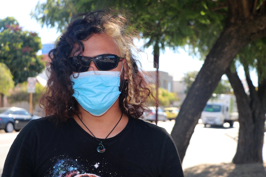 Headshot of a man wearing a face mask standing outside.