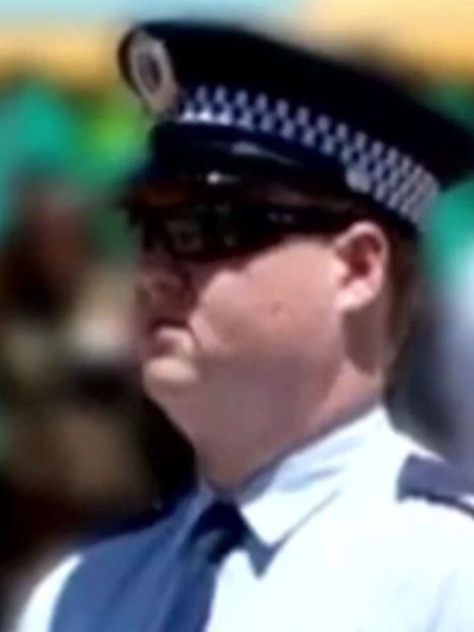 A police officer wearing a hat and sunglasses stands at attention
