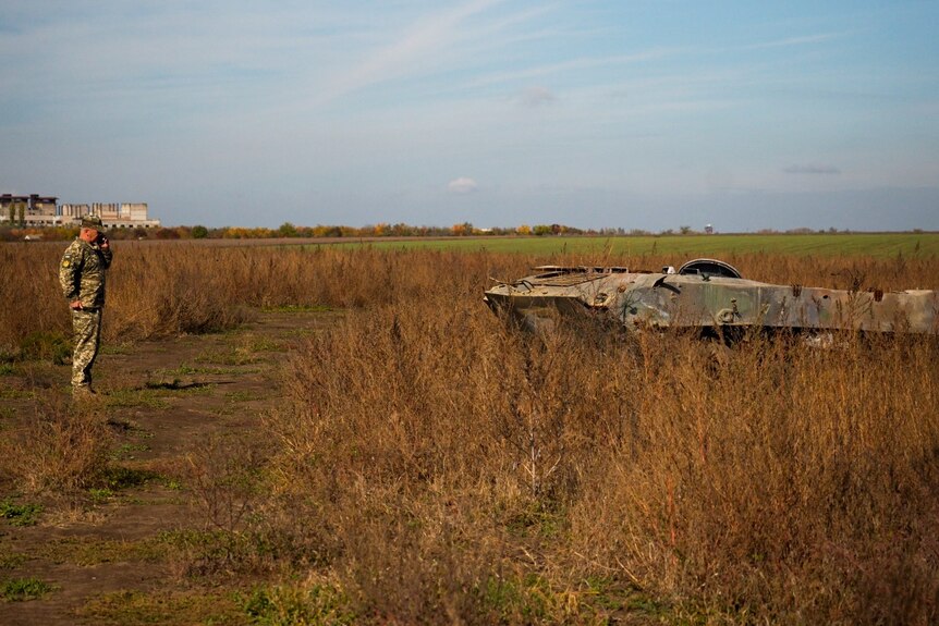 A military official observes a burnt out Russian armoured vehicle outside of Mykolaiv.