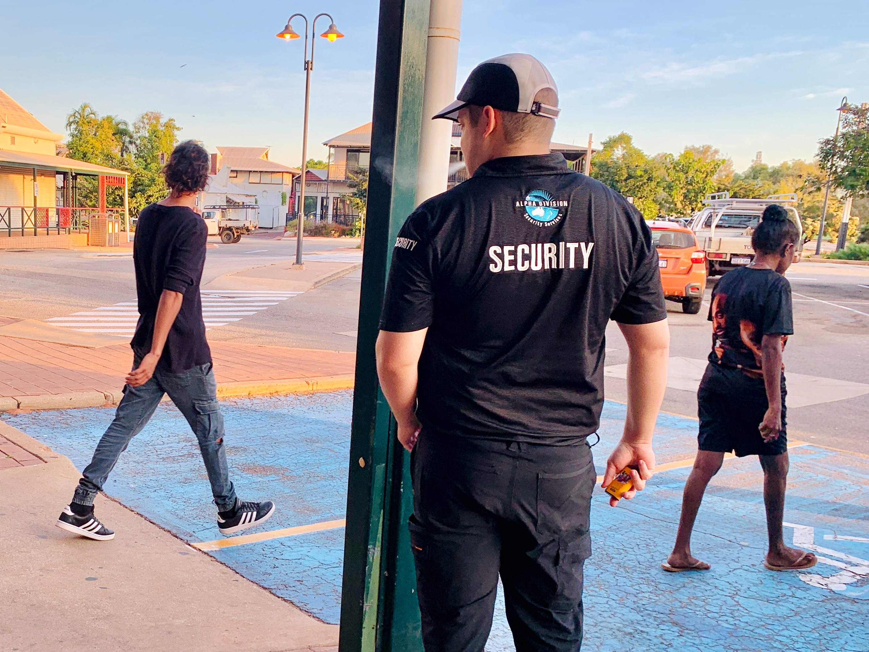 A male security guard stands with his back to the camera as shoppers walk past.