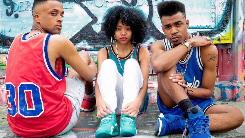 Two men and a woman sit on concrete dressed in sports clothing.