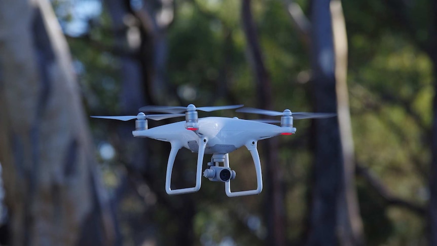 A drone in flight with trees in the background.