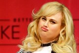 Rebel Wilson pouts in front of a red background.