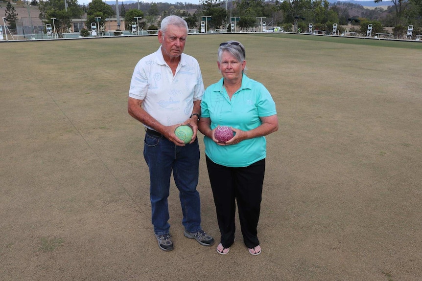 A man and a woman standing on a water-starved bowling green
