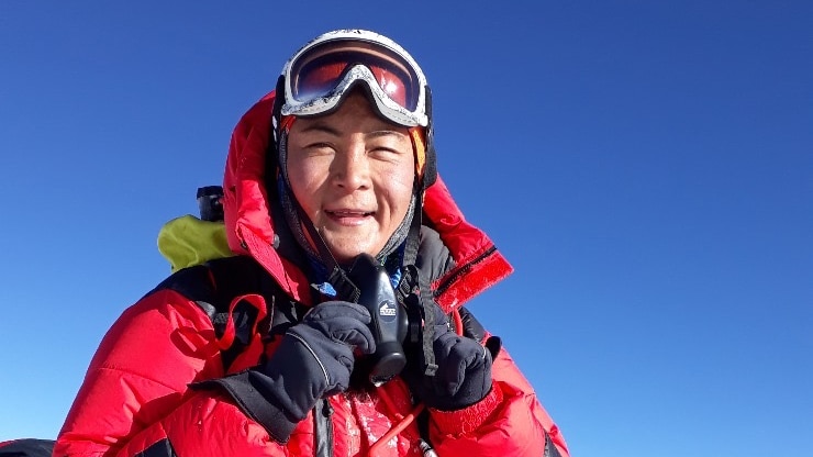 A woman wearing red ski gear and goggles at the top of Mount Everest.