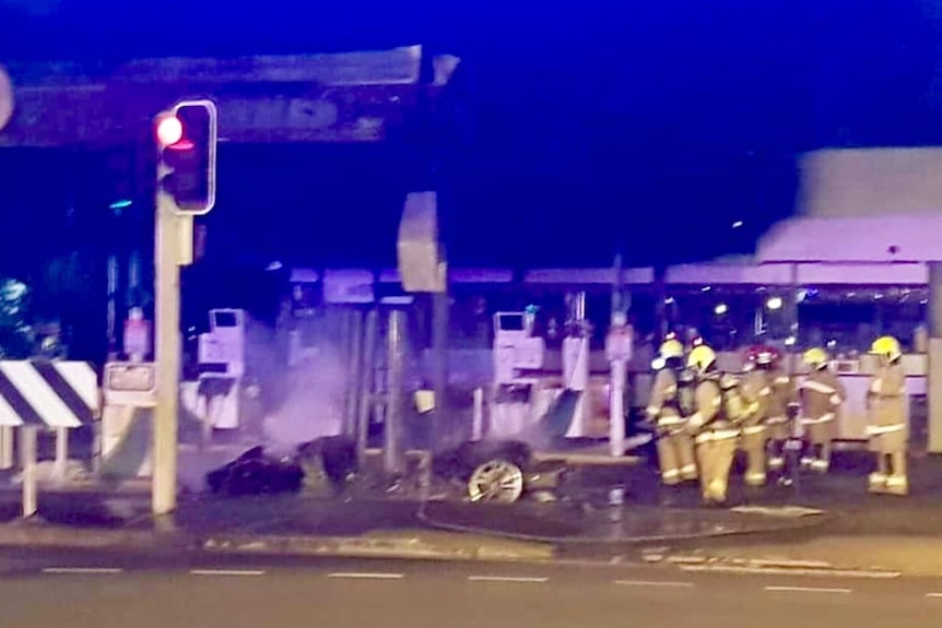 Fire fighters surround the shell of a Corvette which sits at the petrol station.