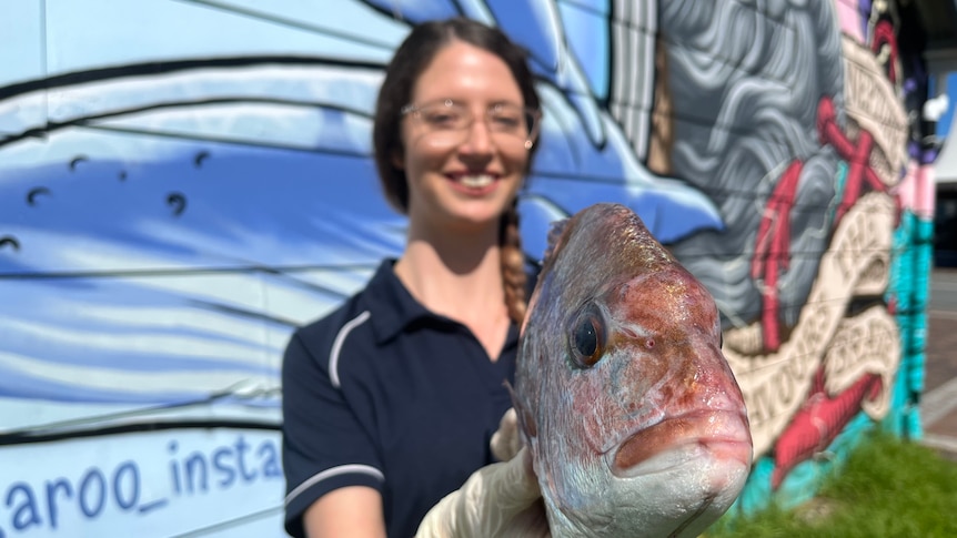 Woman holds a whole fresh fish up toward the camera. 