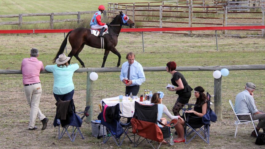 Spectators at their table set up next to the home straight watch a horse make its way to the barrier.