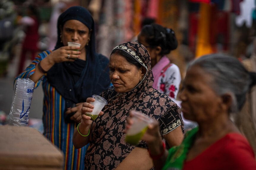 Shoppers drink juice in plastic glasses at a market stall.