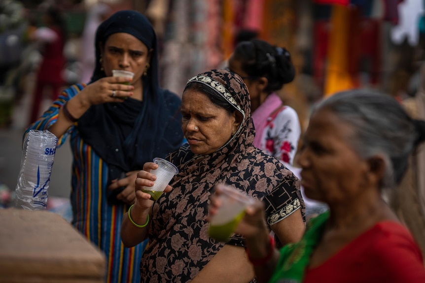 Shoppers drink juice in plastic glasses at a market stall.