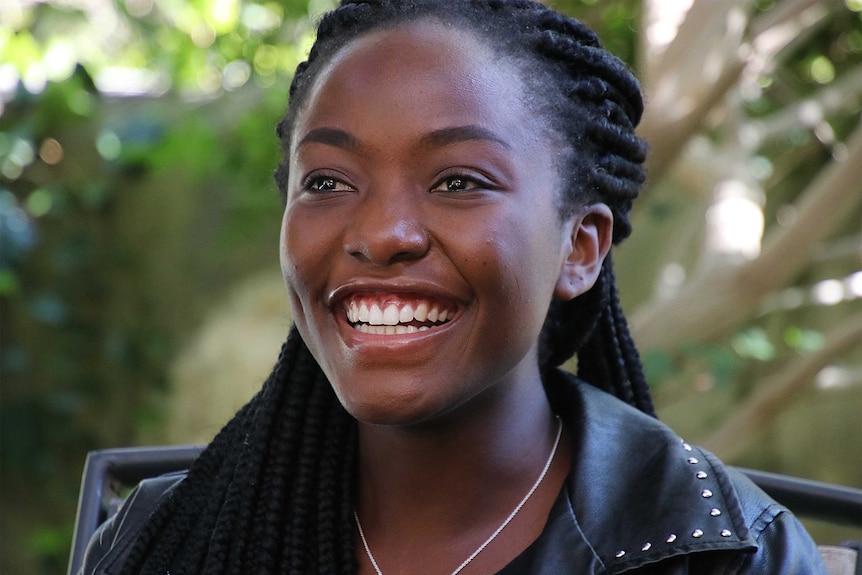 A smiling woman with plaited hair and wearing a leather jacket.